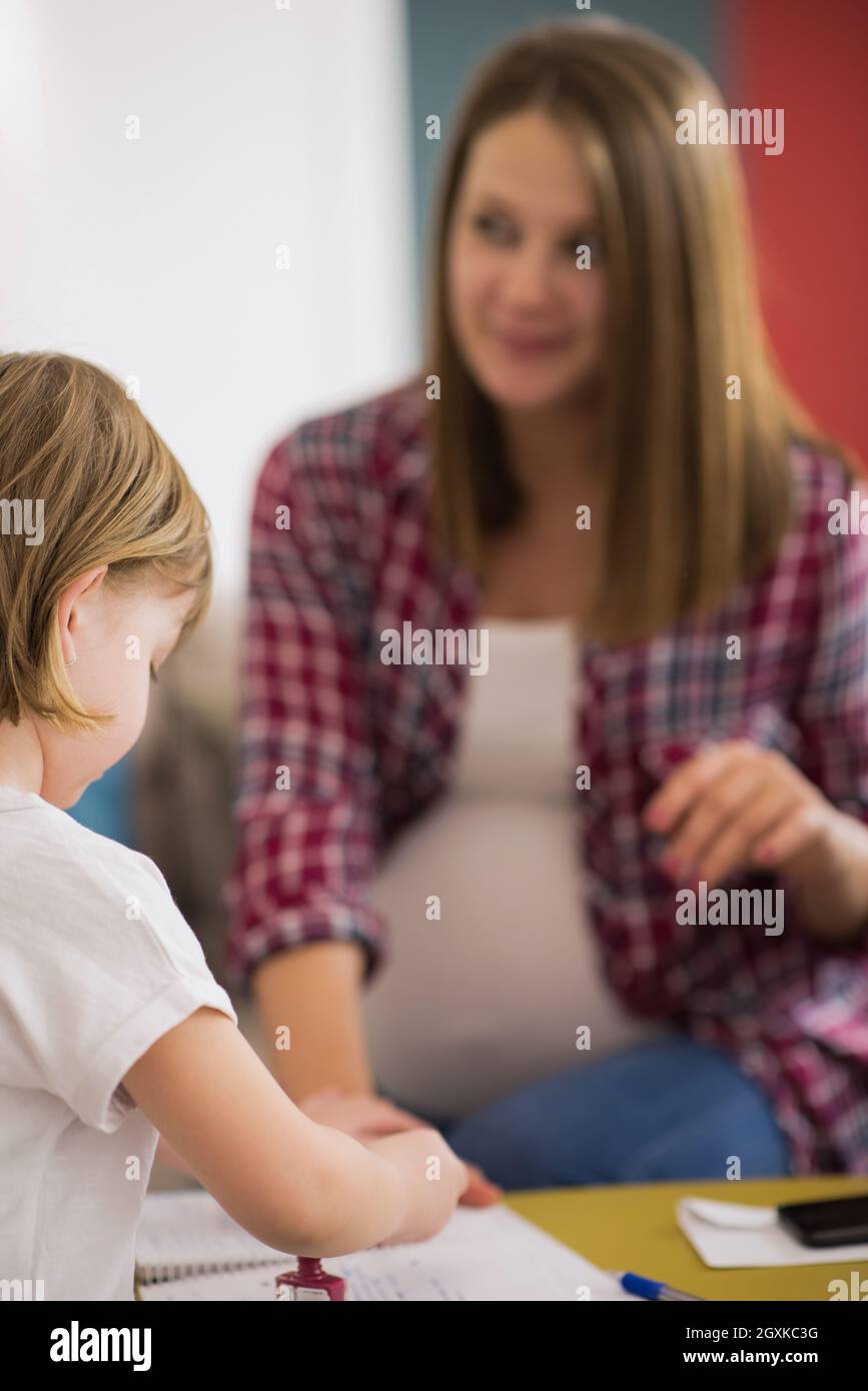 little cute daughter painting nails to her pregnant mom while relaxing