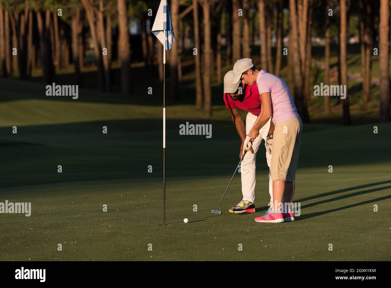 male golf instructor teaching female golf player, personal trainer giving lesson on golf course