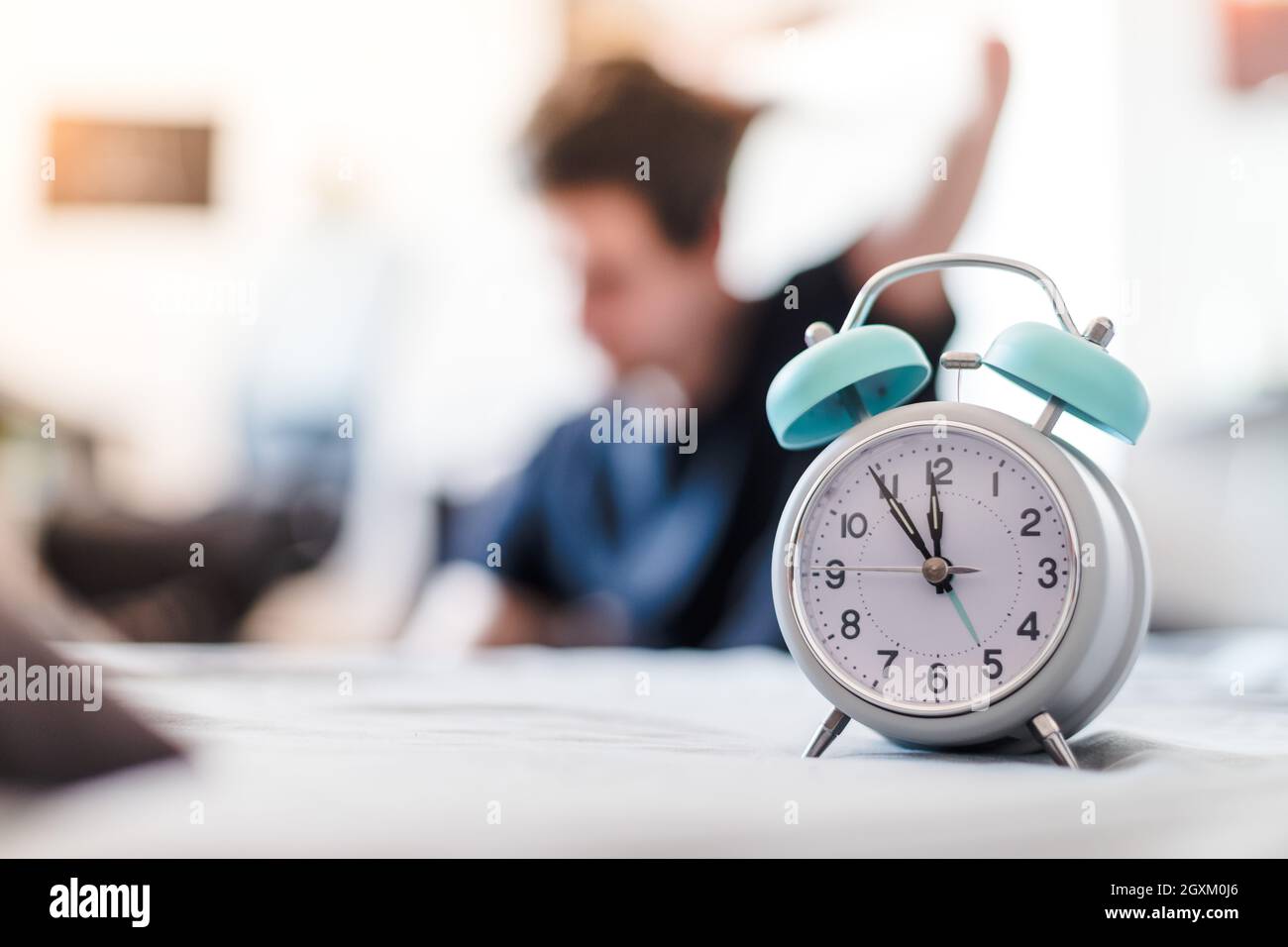 White alarm clock in the morning. Young man wakes up and stretches in