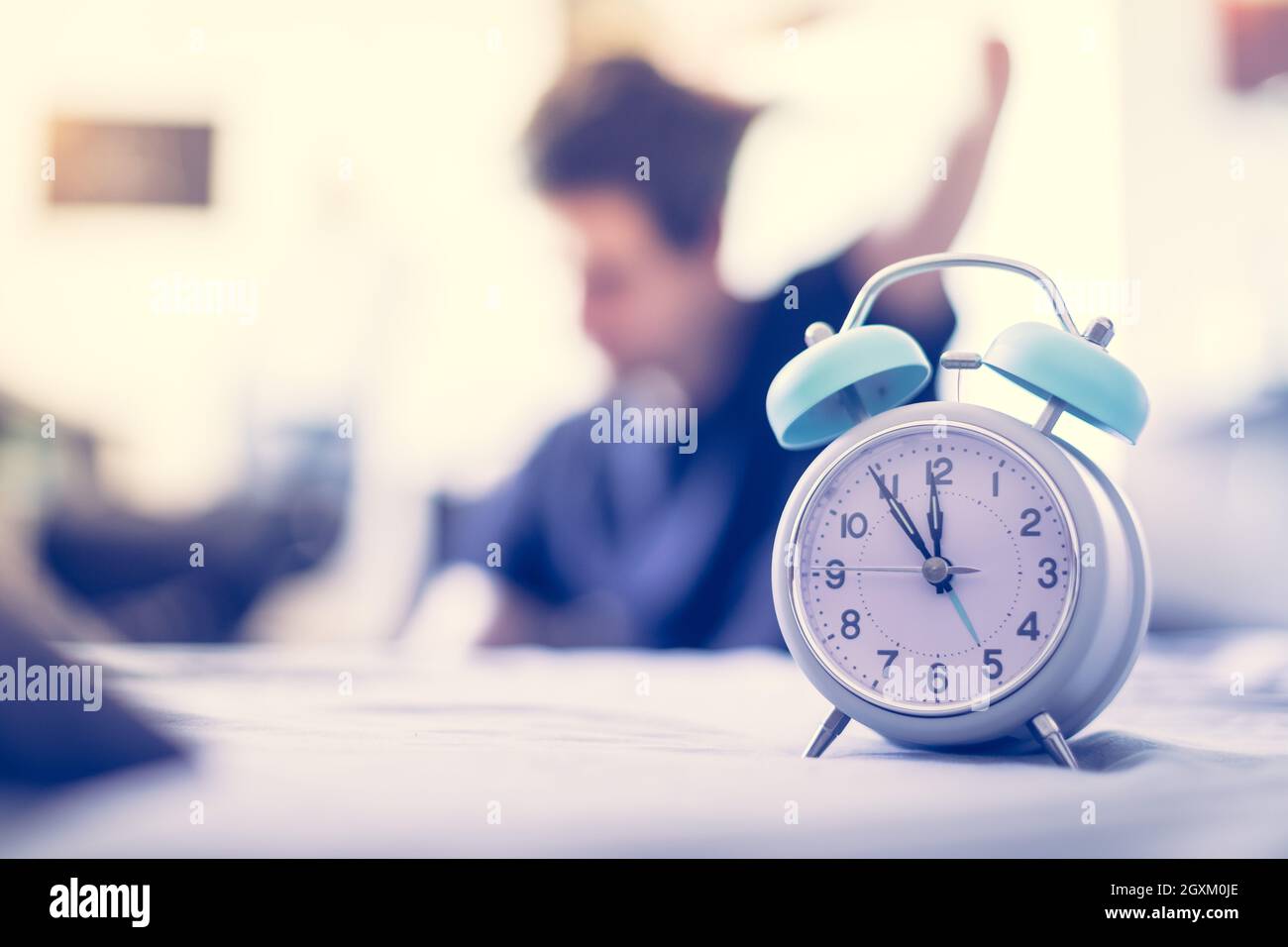 White alarm clock in the morning. Young man wakes up and stretches in the background Stock Photo