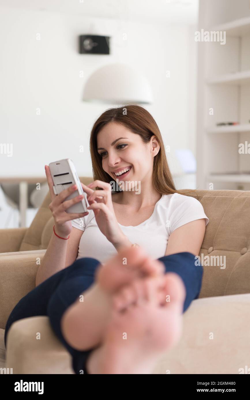 young happy woman sitting on sofa with mobile phone at luxury home ...
