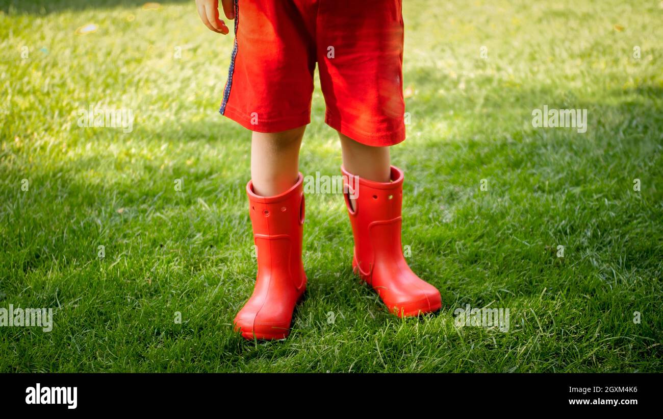 Closeup photo of child wearing red rubber boots standing on grass at ...