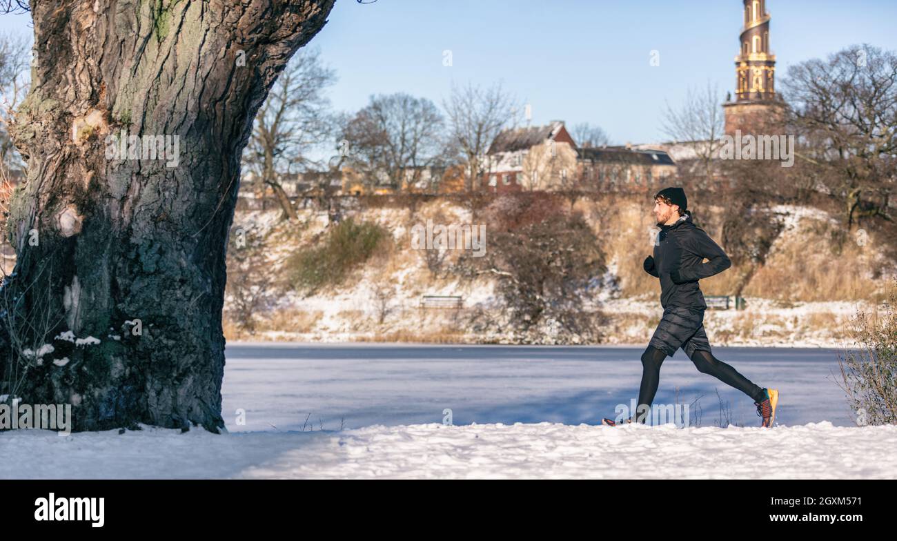 Winter run active healthy lifestyle man runner jogging outdoors in cold weather clothes jacket and leggings. Panoramic banner of jogger training Stock Photo