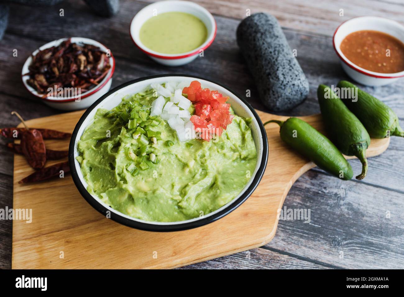 Bowl of Guacamole next to fresh ingredients on a wooden table in Mexico Stock Photo