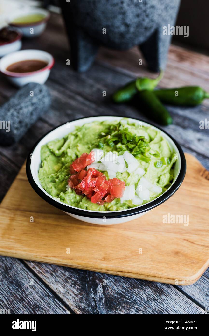 Bowl of Guacamole next to fresh ingredients on a wooden table in Mexico Stock Photo