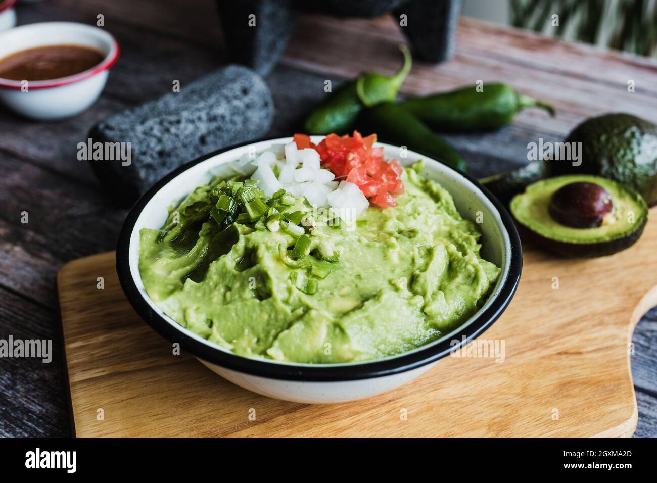 Bowl of Guacamole next to fresh ingredients on a wooden table in Mexico Stock Photo