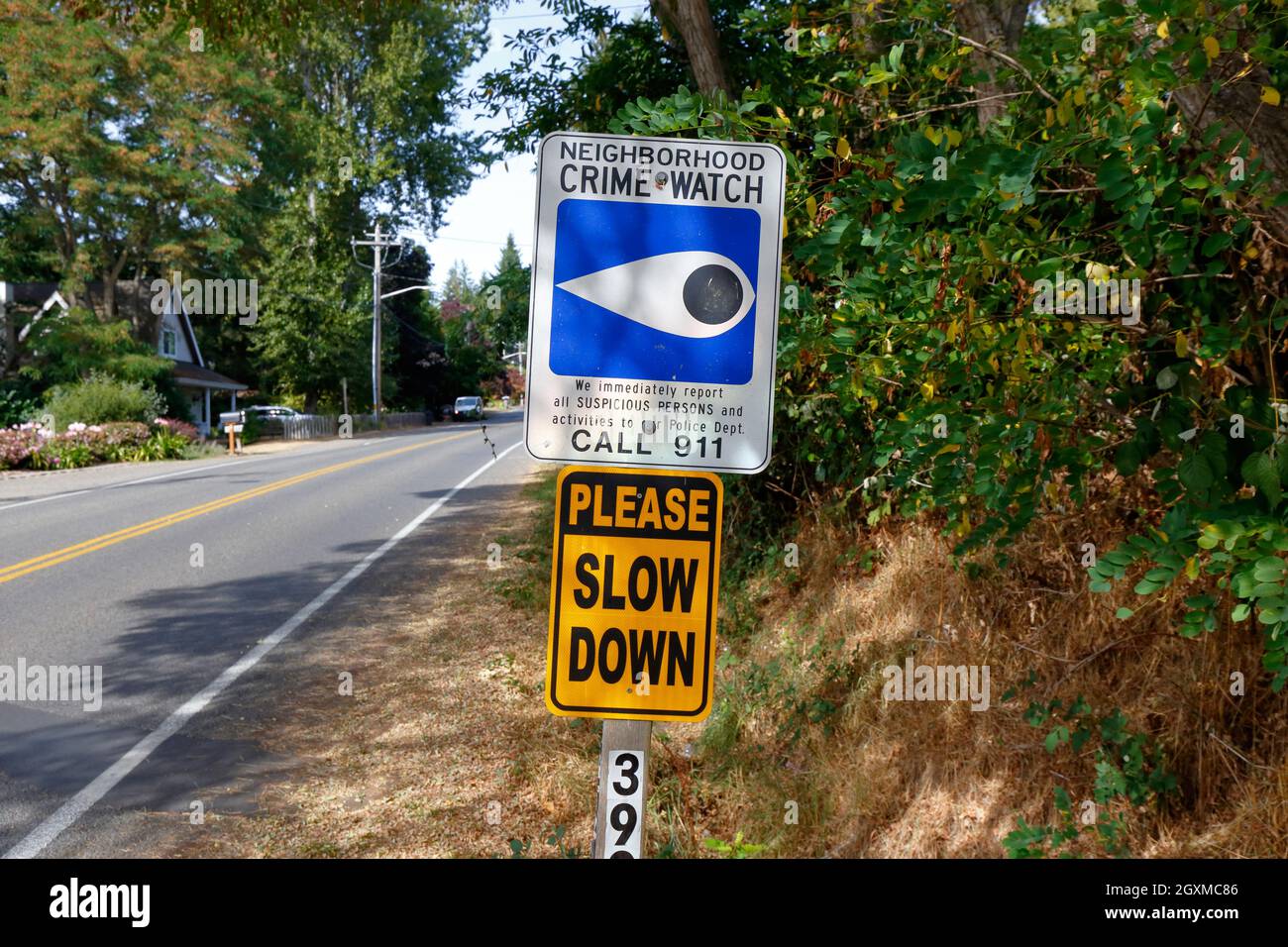 A Neighborhood Crime Watch sign, and a Please Slow Down sign mounted on a pole by a roadside. Stock Photo