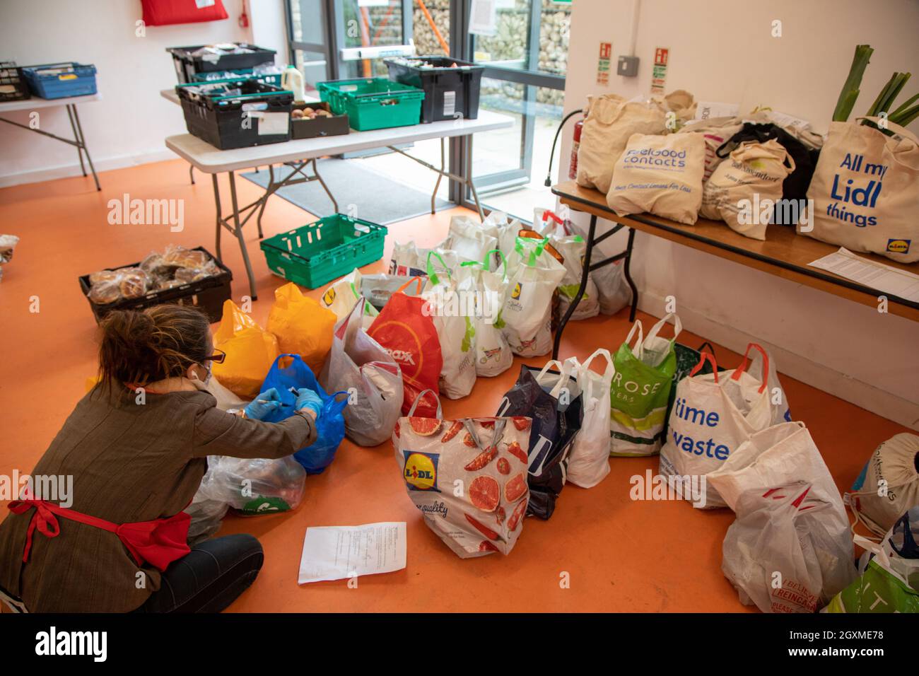 A woman volunteer at a food bank sorting bags  of donated food in preparation for distributing to members of the local community in need.  They are at Stock Photo
