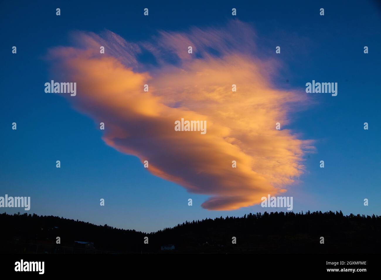 Large pink and white cloud in blue sky with mountain silhouette Stock Photo