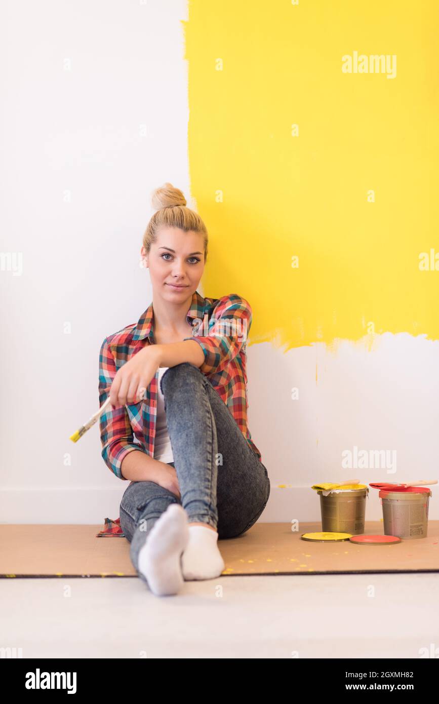 Portrait of a beautiful young female painter sitting on floor near wall ...