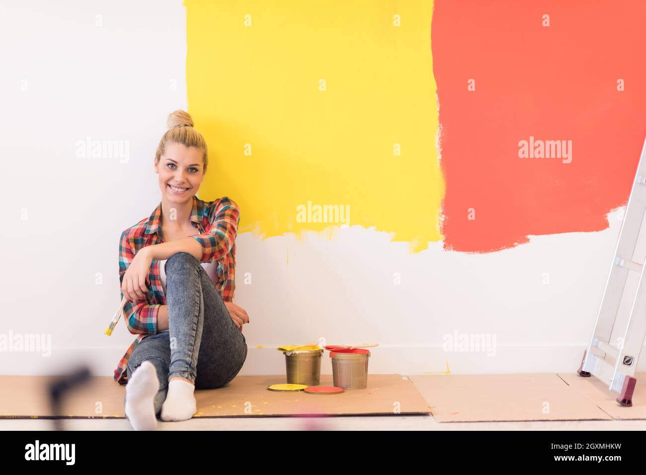 Portrait of a beautiful young female painter sitting on floor near wall ...