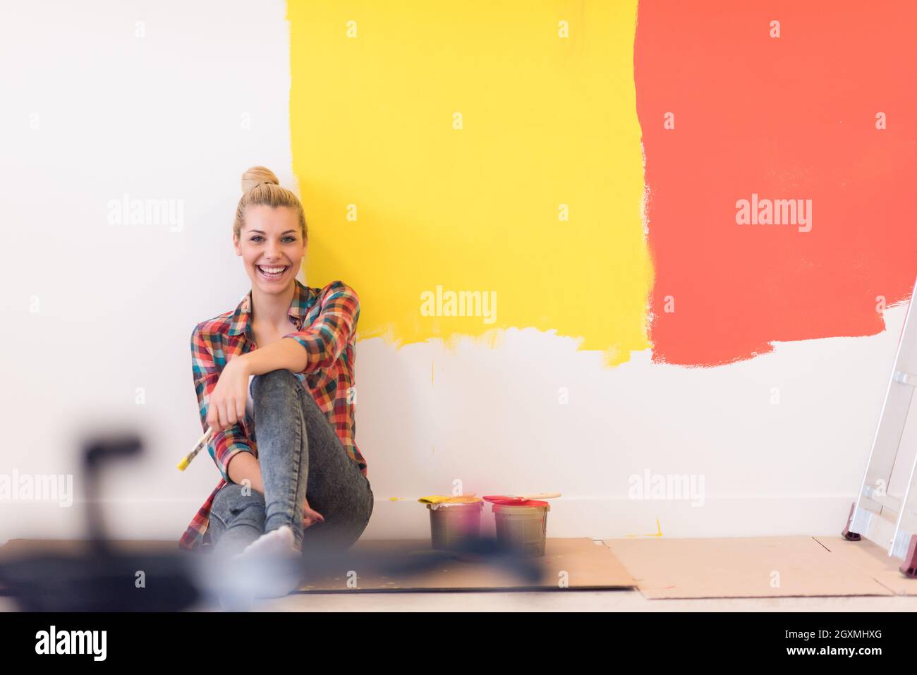 Portrait of a beautiful young female painter sitting on floor near wall ...
