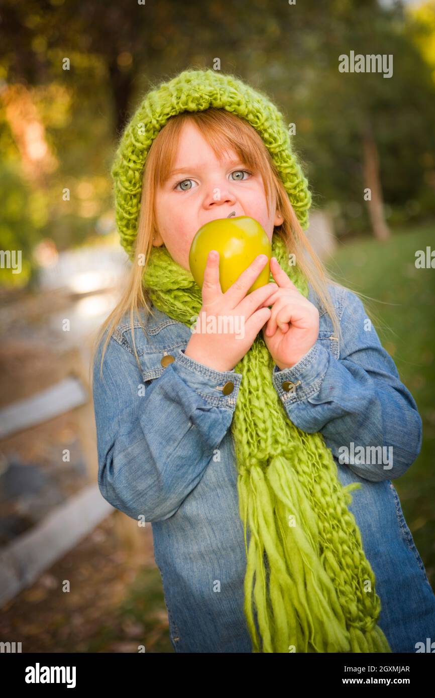 Cute Smiling Young Girl Wearing Green Scarf and Hat Eating A Green