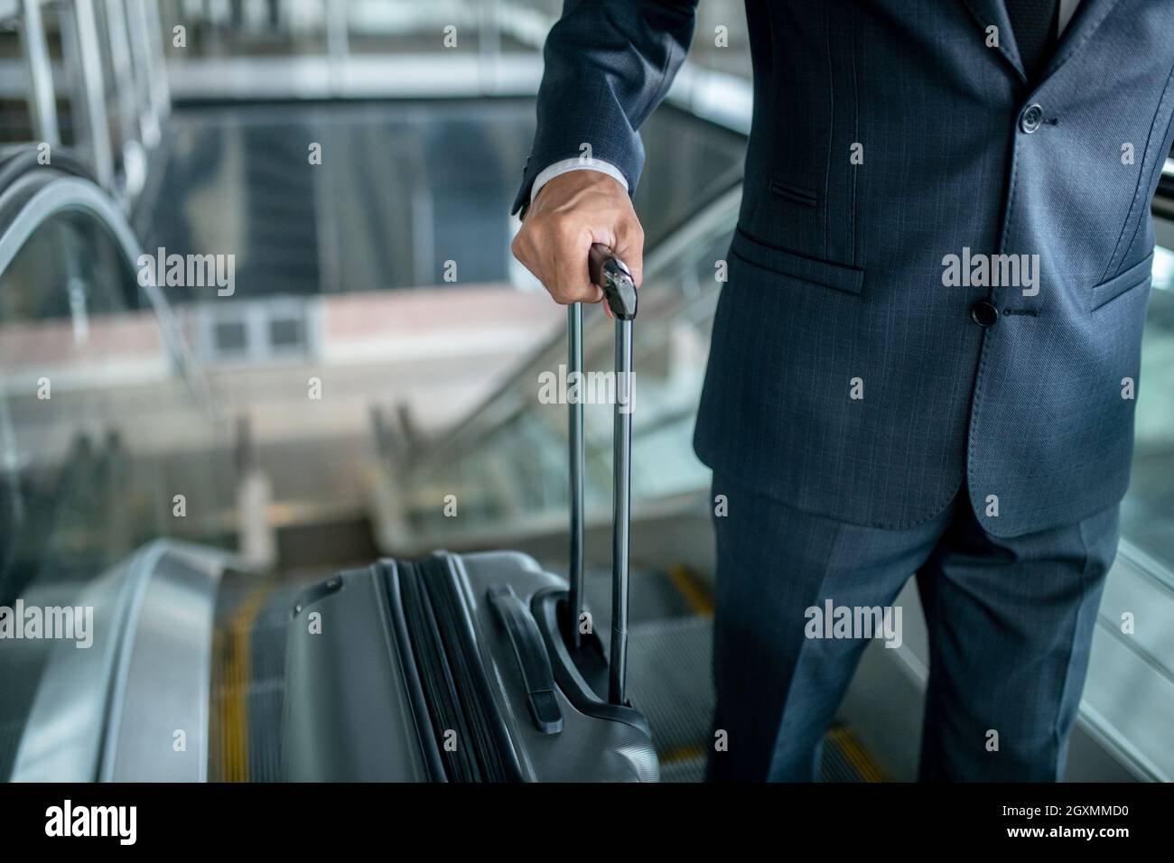 Man holding suitcase on escalator going up Stock Photo