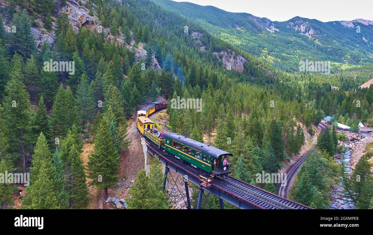Locomotive train with passengers going through pine trees in mountain Stock Photo
