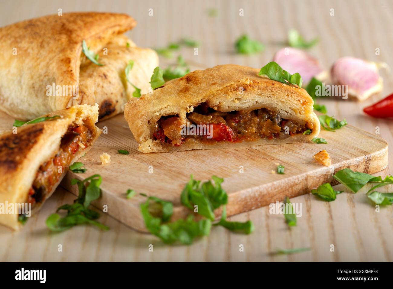 Puff pastry filled with vegetables on wooden cutting board with herbs - close up view Stock Photo