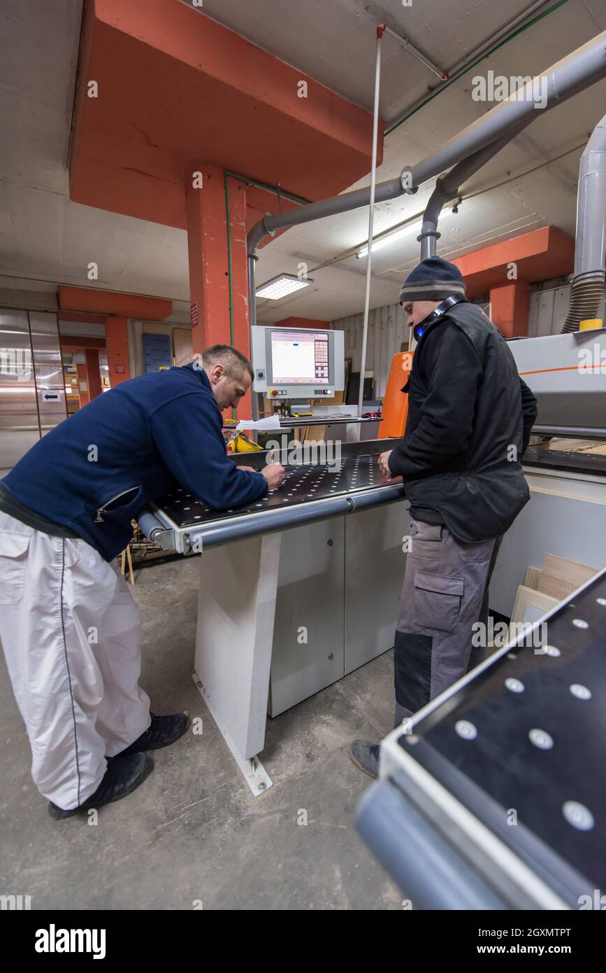 two young carpenters calculating and programming a cnc wood working machine in workshop. wood workers preparing a computer program for CNC machine at Stock Photo