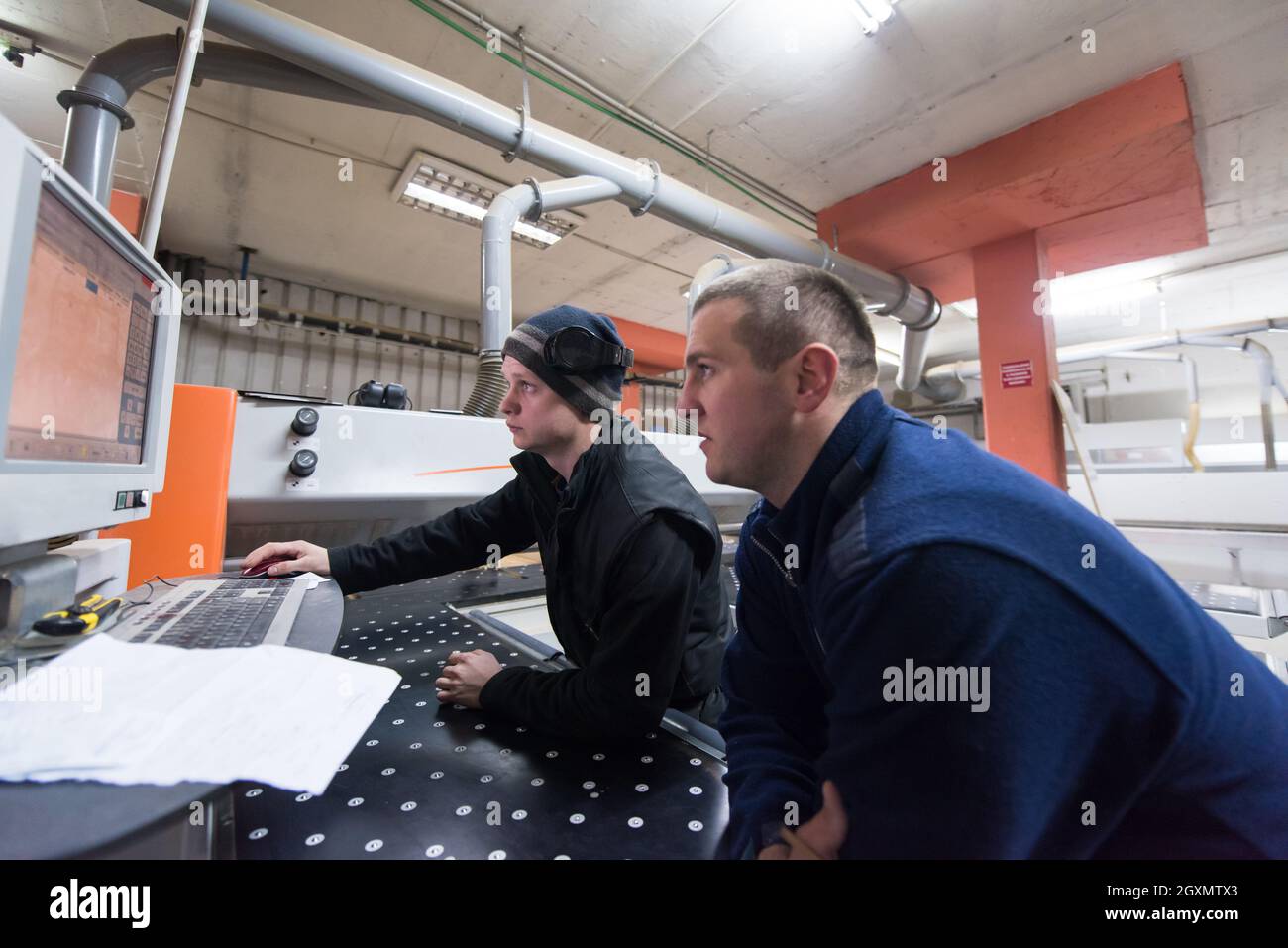 two young carpenters calculating and programming a cnc wood working machine in workshop. wood workers preparing a computer program for CNC machine at Stock Photo