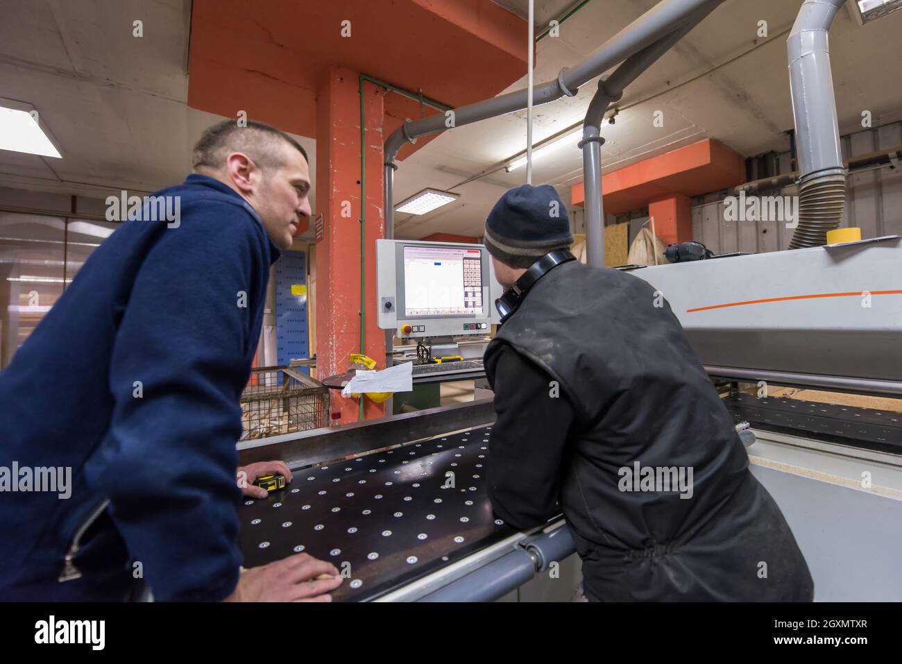 two young carpenters calculating and programming a cnc wood working machine in workshop. wood workers preparing a computer program for CNC machine at Stock Photo