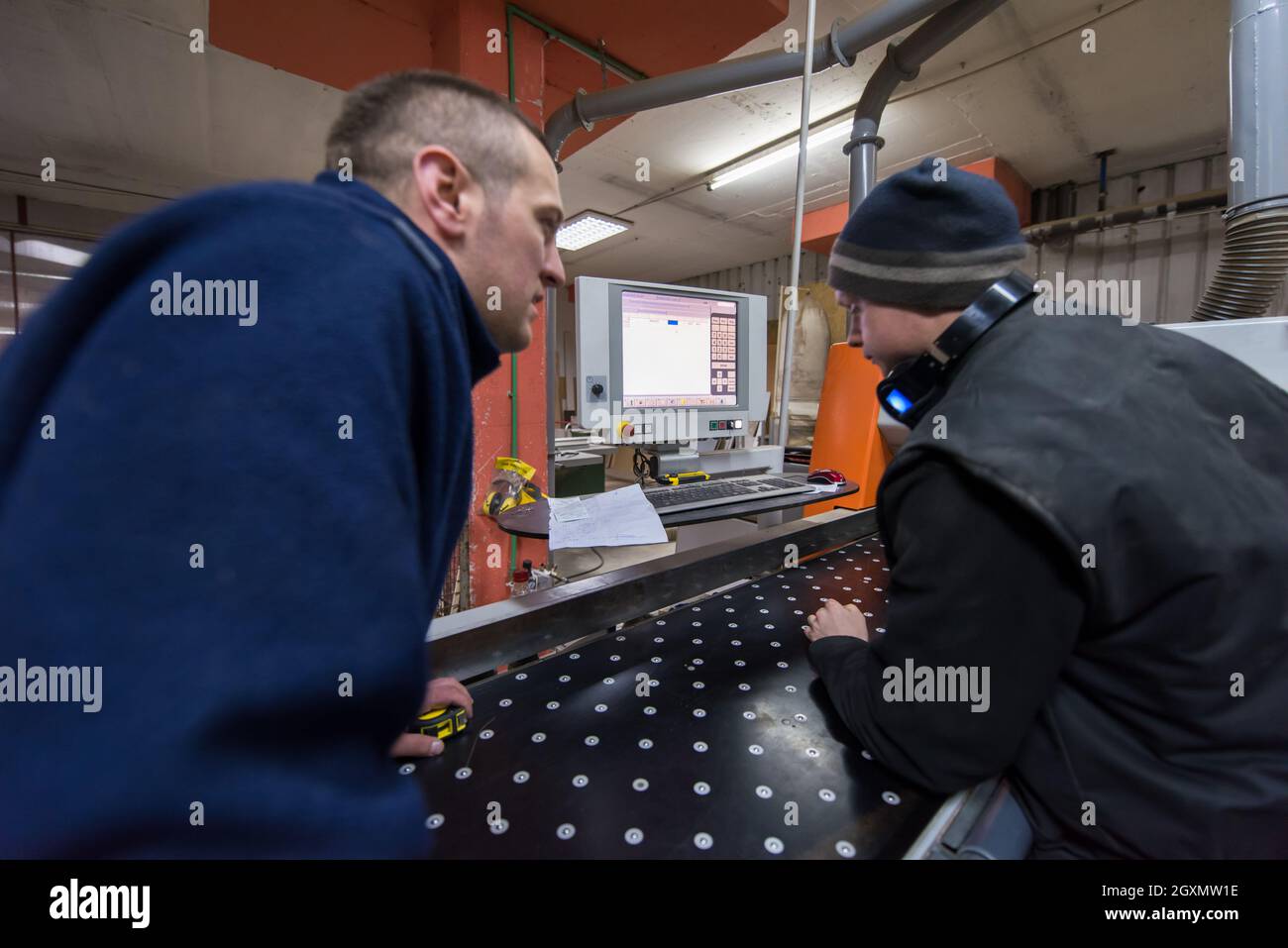 two young carpenters calculating and programming a cnc wood working machine in workshop. wood workers preparing a computer program for CNC machine at Stock Photo