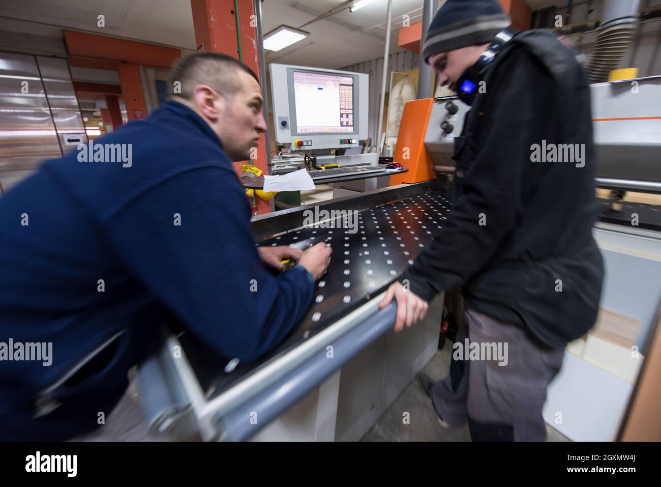 two young carpenters calculating and programming a cnc wood working machine in workshop. wood workers preparing a computer program for CNC machine at Stock Photo
