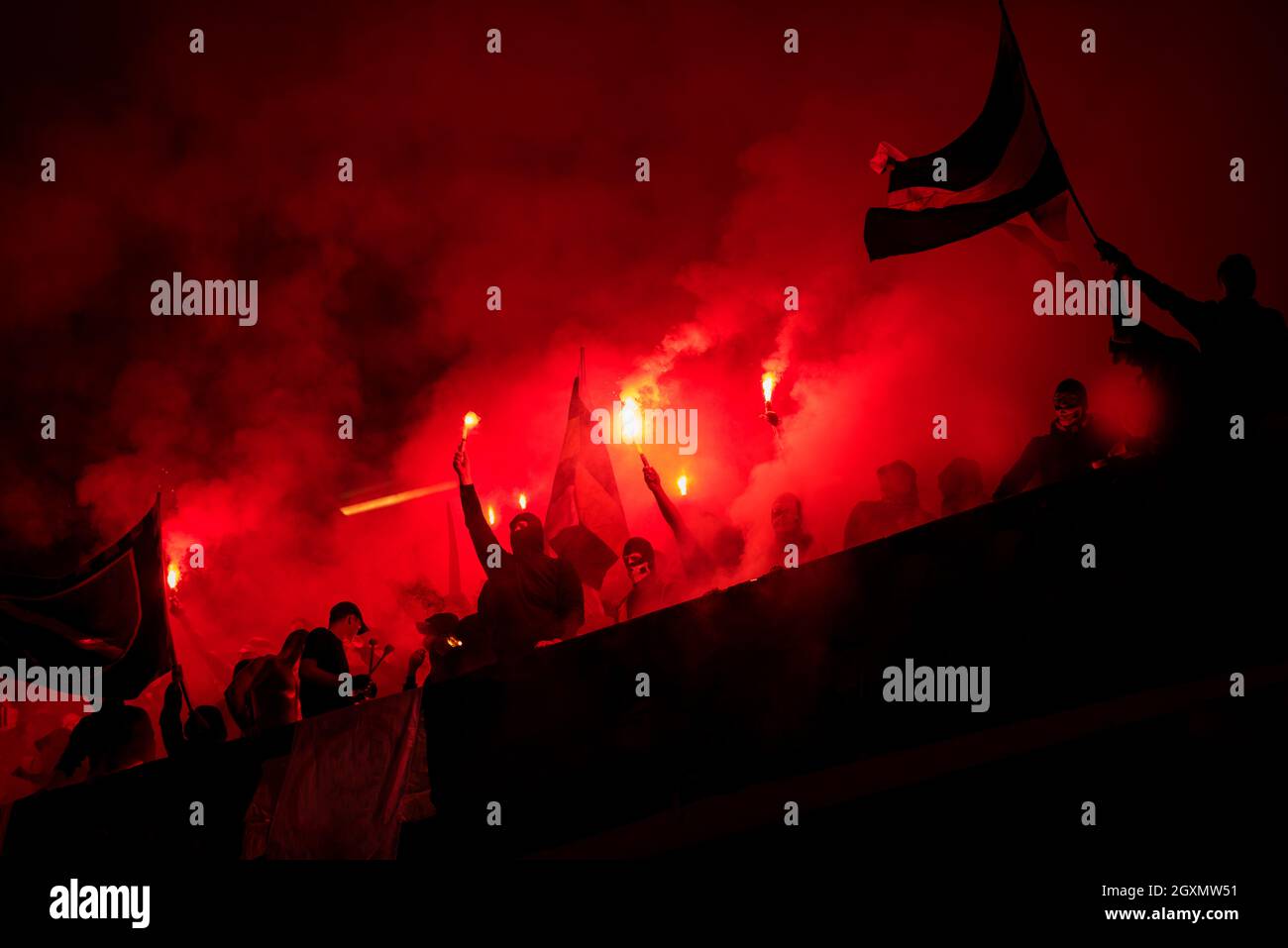 football hooligans with mask holding torches in fire while supporting their favorite team during a match at stadium Stock Photo
