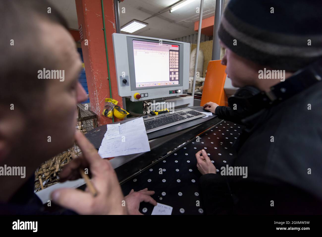 two young carpenters calculating and programming a cnc wood working machine in workshop. wood workers preparing a computer program for CNC machine at Stock Photo