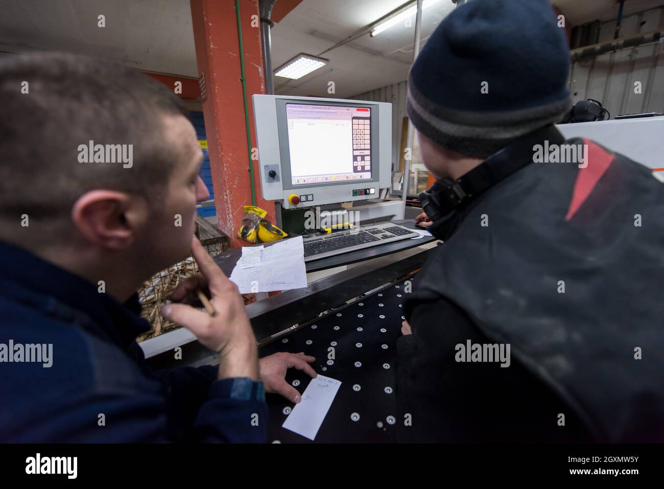 two young carpenters calculating and programming a cnc wood working machine in workshop. wood workers preparing a computer program for CNC machine at Stock Photo