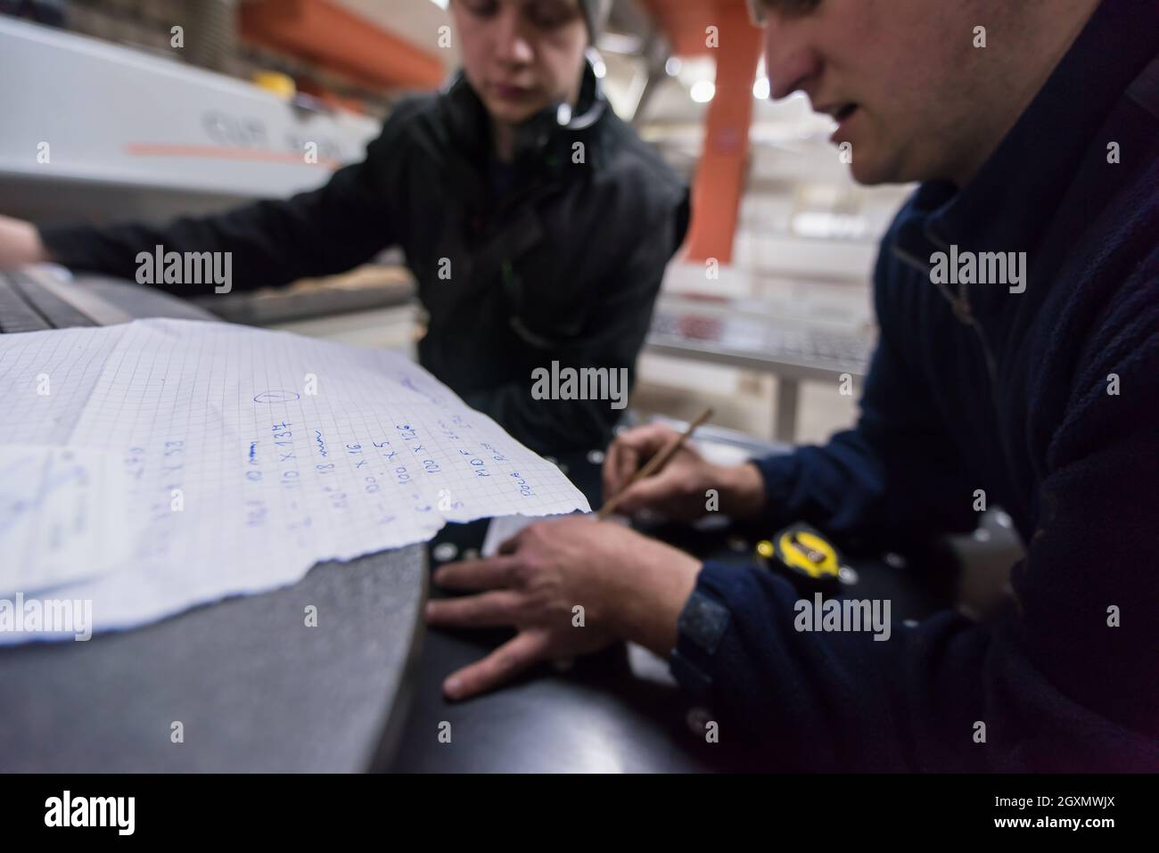 two young carpenters calculating and programming a cnc wood working machine in workshop. wood workers preparing a computer program for CNC machine at Stock Photo