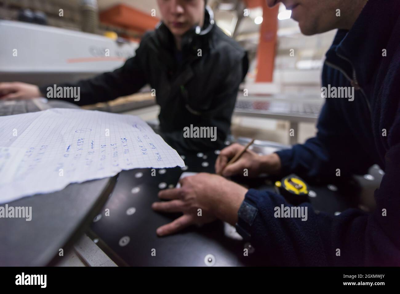 two young carpenters calculating and programming a cnc wood working machine in workshop. wood workers preparing a computer program for CNC machine at Stock Photo