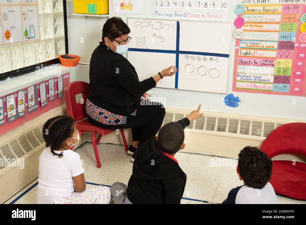 Education Preschool 4-5 year olds morning meeting, boy pointing to answer question, teacher and children wearing face masks to protect vs Covid-19 Stock Photo