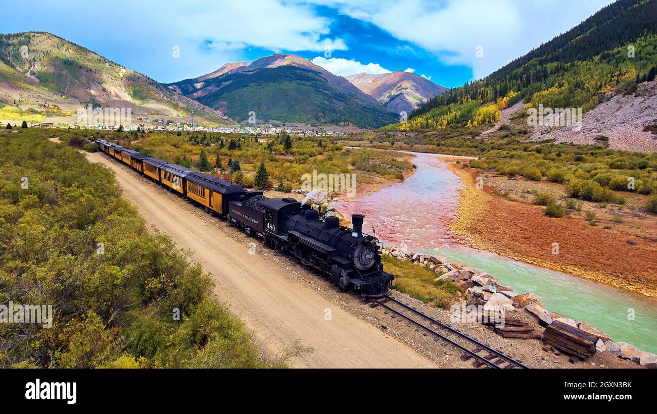 Majestic train leaving mining town along river and surrounded by mountains Stock Photo