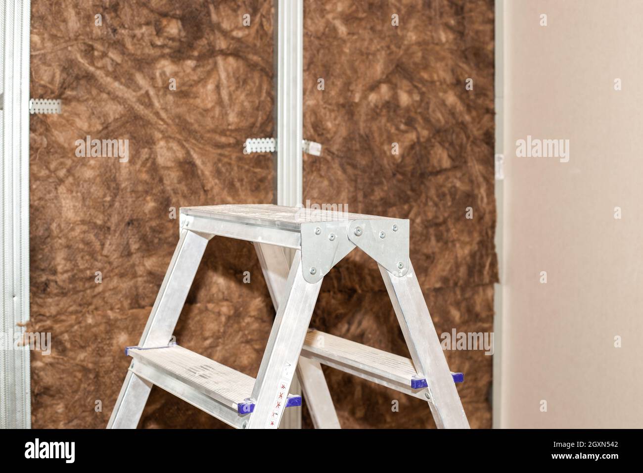 Home repairs. A folding ladder stands against the background of a wall lined with mineral wool for further cladding with plasterboard. Heat insulation Stock Photo