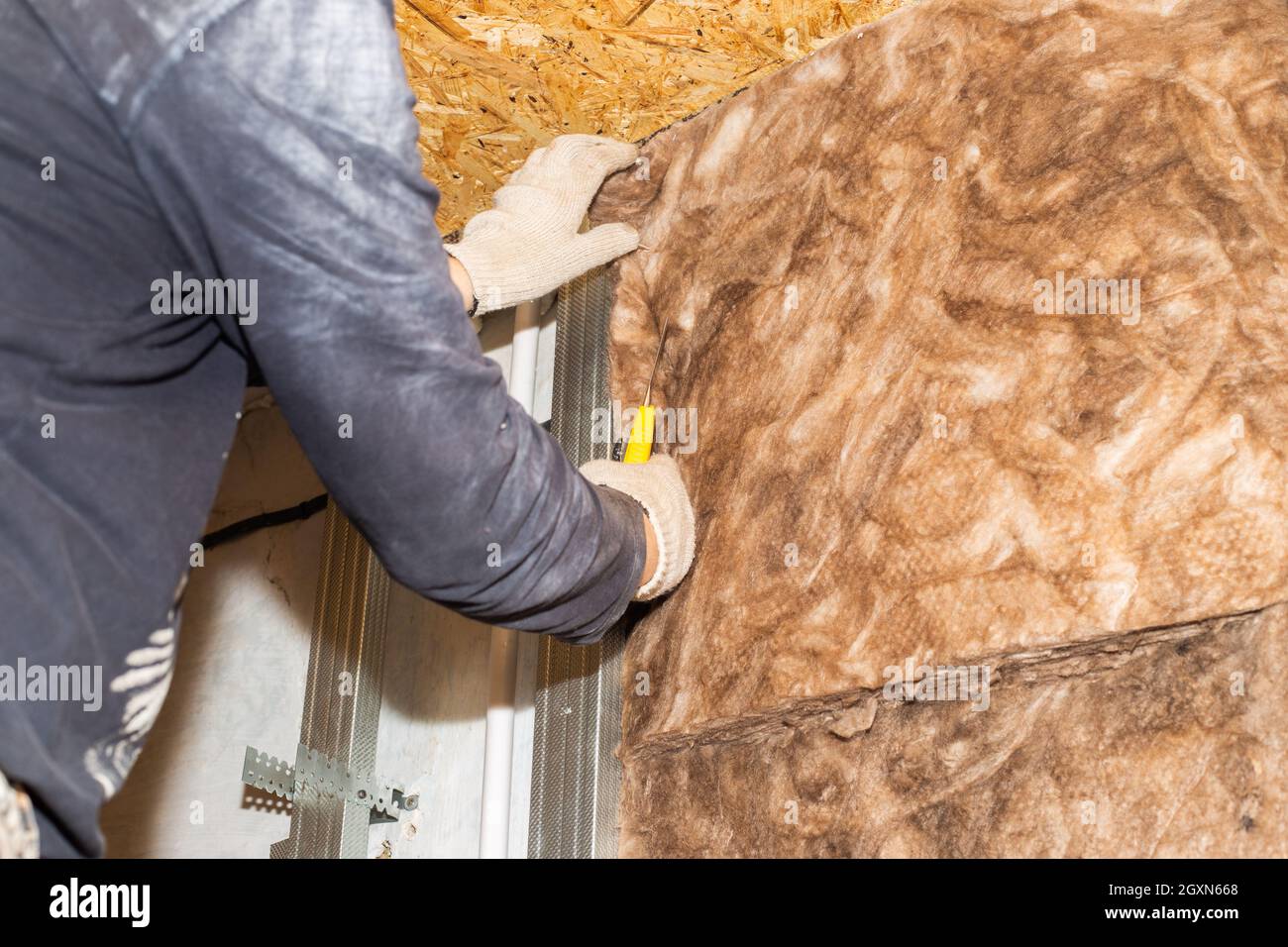 The worker attaches mineral wool to the walls for further plasterboard cladding. Thermal insulation and sound insulation of housing. Home renovation. Stock Photo