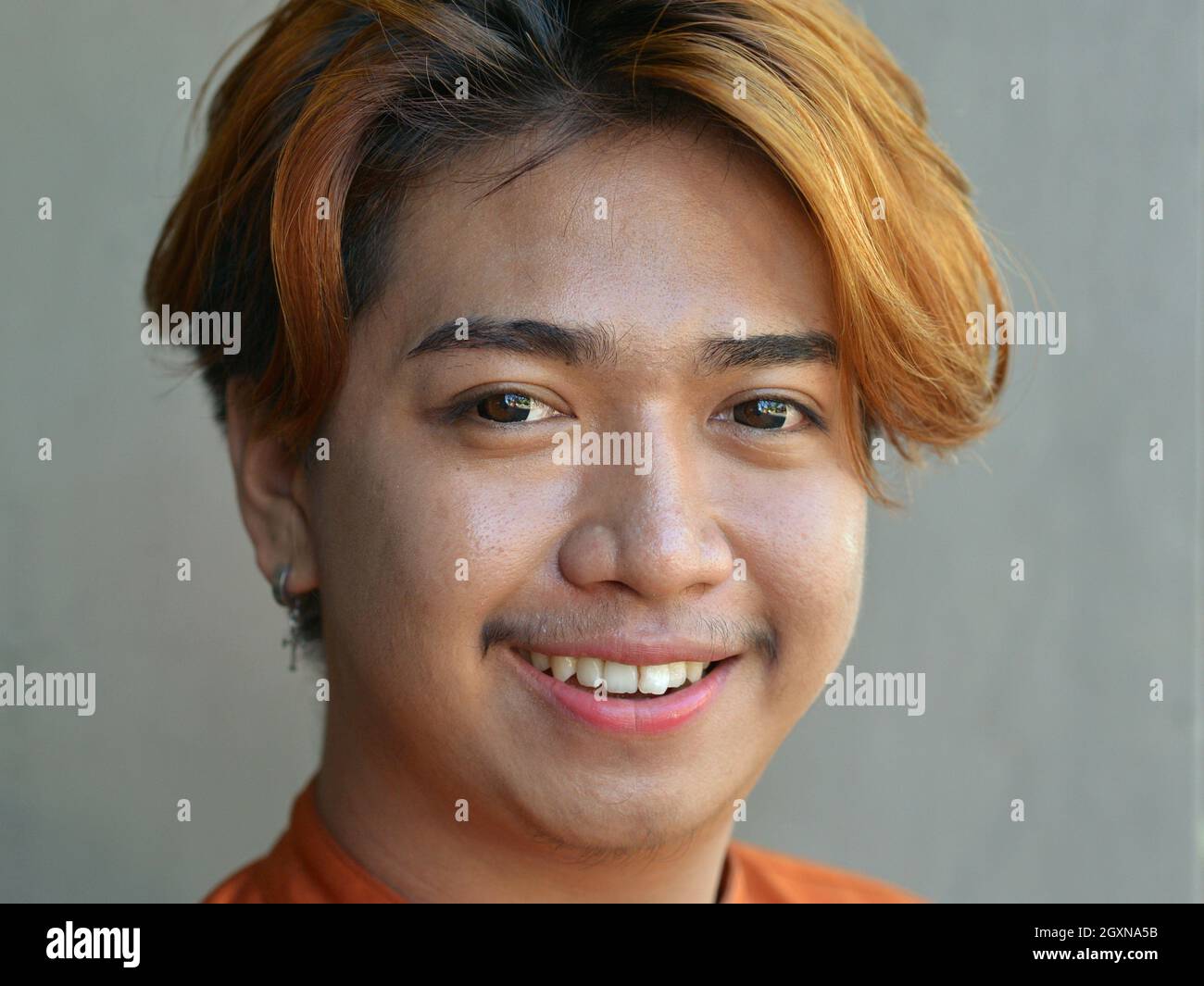 Positive optimistic young male Indonesian Balinese massage therapist with dyed hair and contact lenses smiles for the camera. Stock Photo