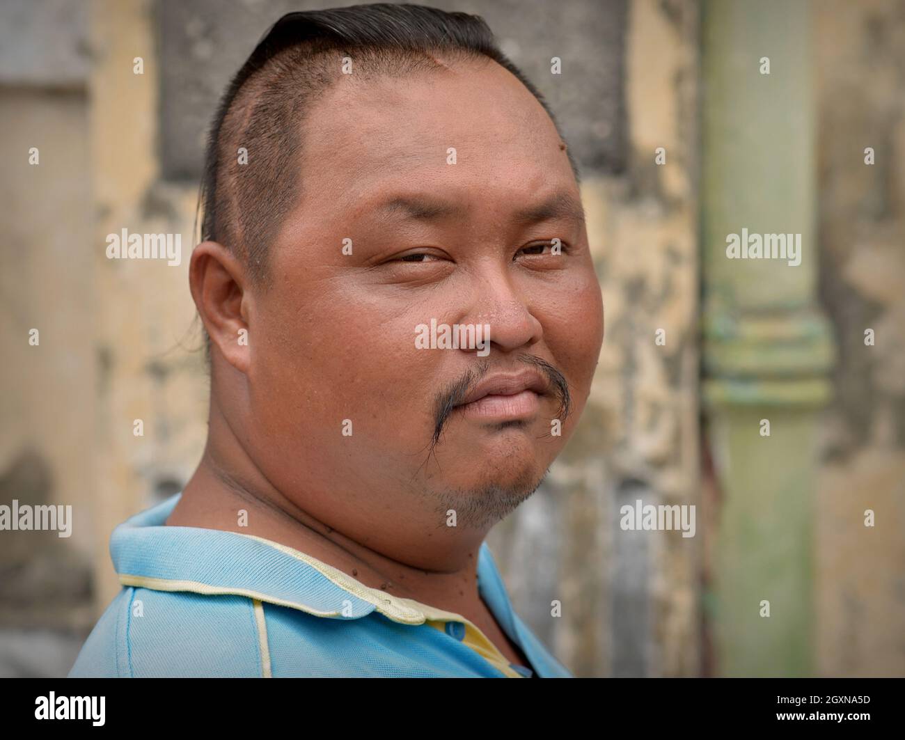 Disgusted chubby young Malaysian Chinese trishaw driver with Chinese moustache and modern short sides long top haircut looks at the viewer. Stock Photo