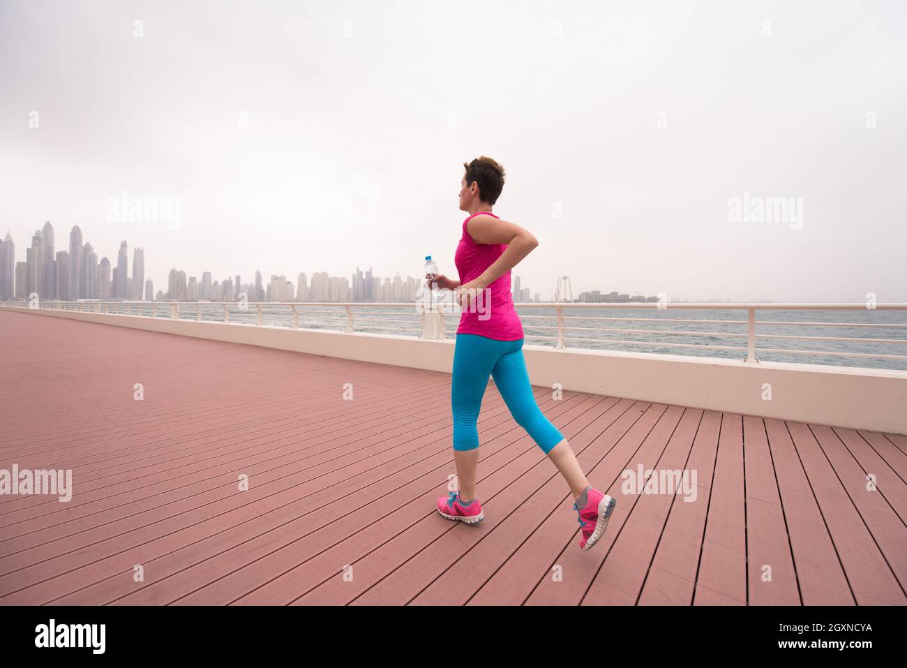 very active young beautiful woman busy running on the promenade along ...