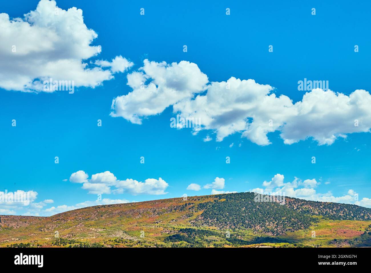 Blue sky with small clouds against colorful hill Stock Photo