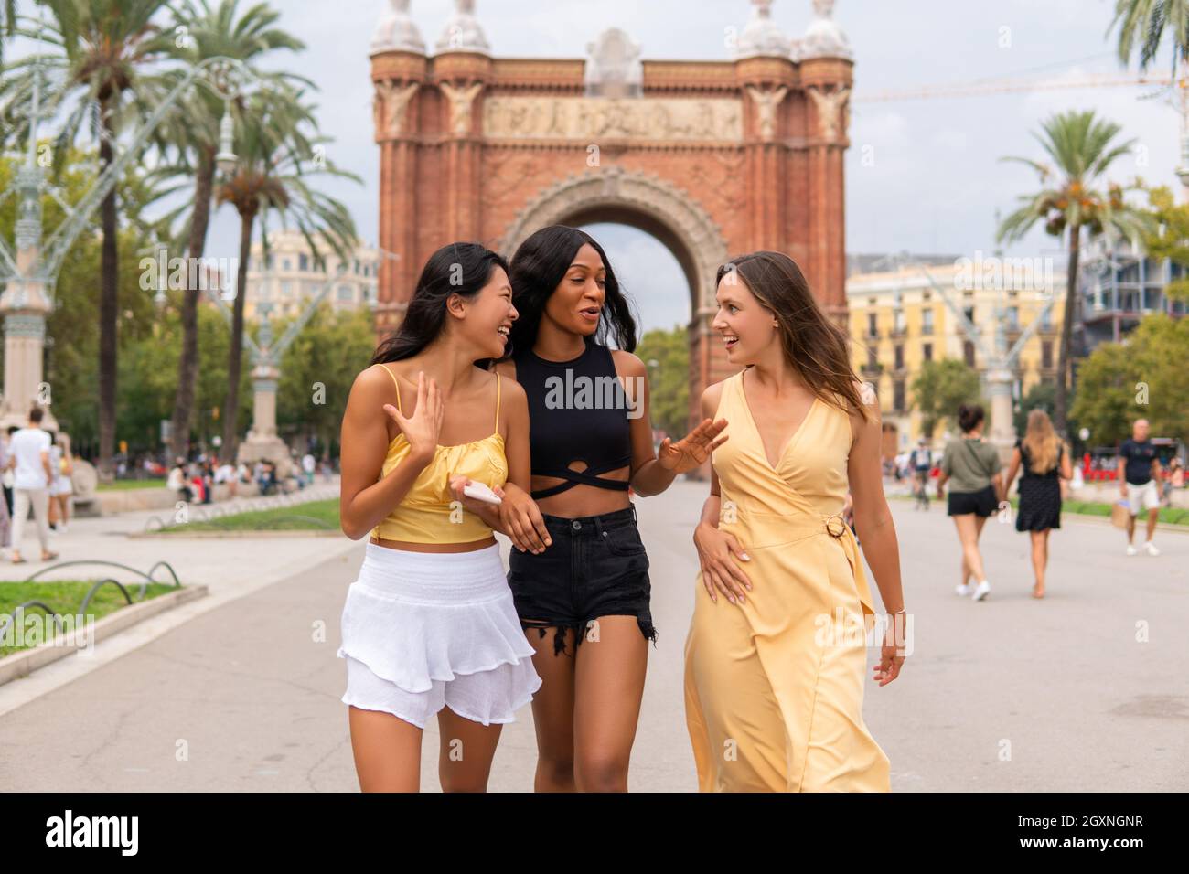 Group of excited young female friends sharing impressions after sightseeing tour and laughing happily while visiting Barcelona city during summer holidays Stock Photo