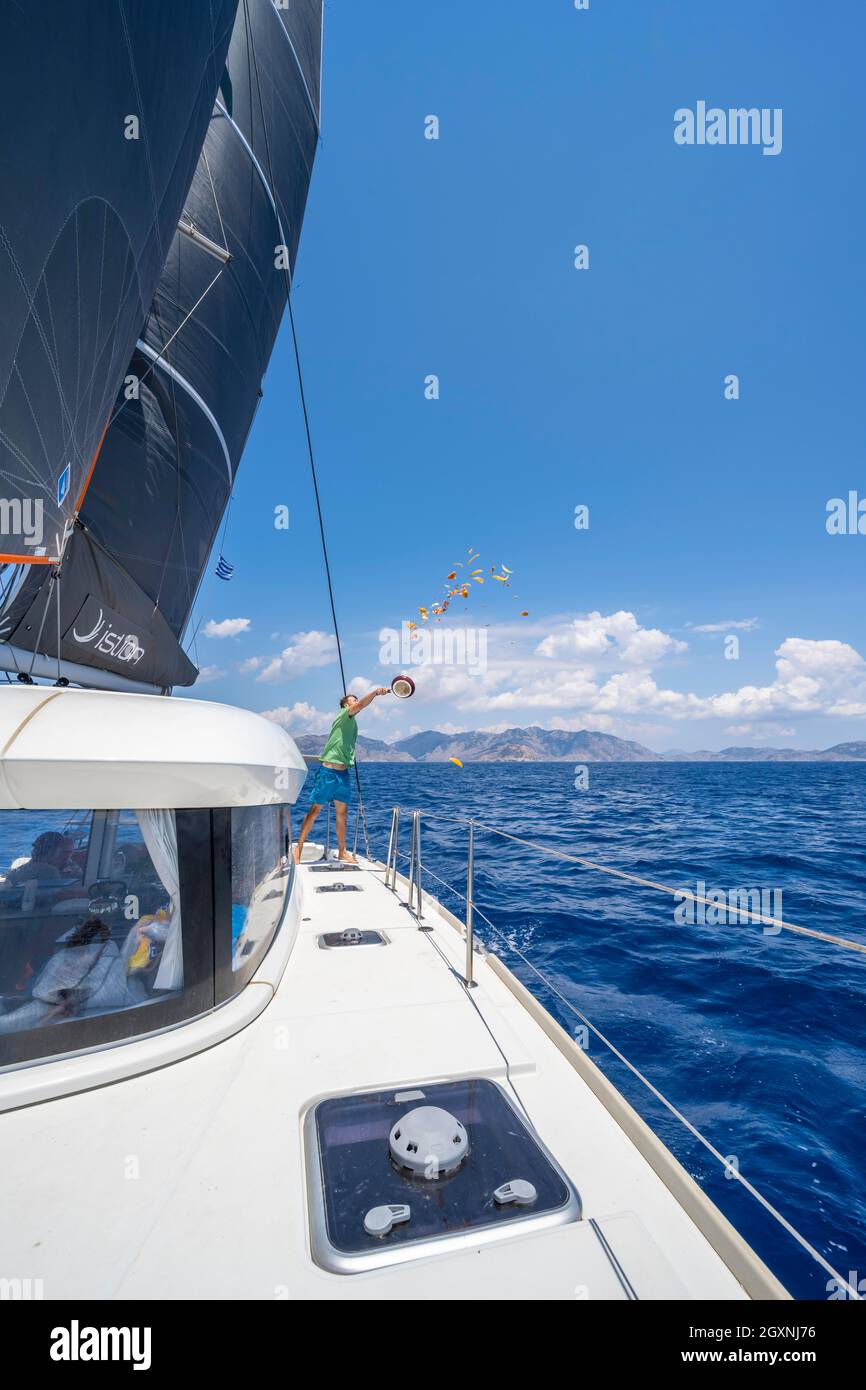 Young man throws food scraps overboard, sailing on a catamaran, Dodecanese, Greece Stock Photo