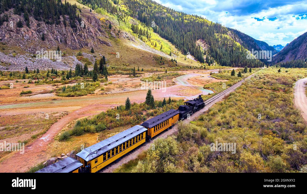 Old black train with coal going through valley surrounded by mountains Stock Photo