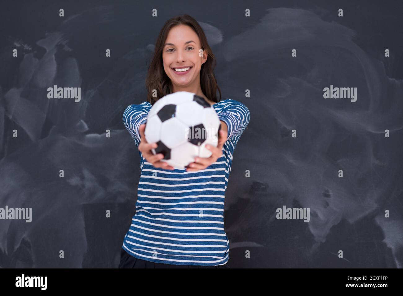 portrait of a young woman holding a soccer ball in front of chalk ...