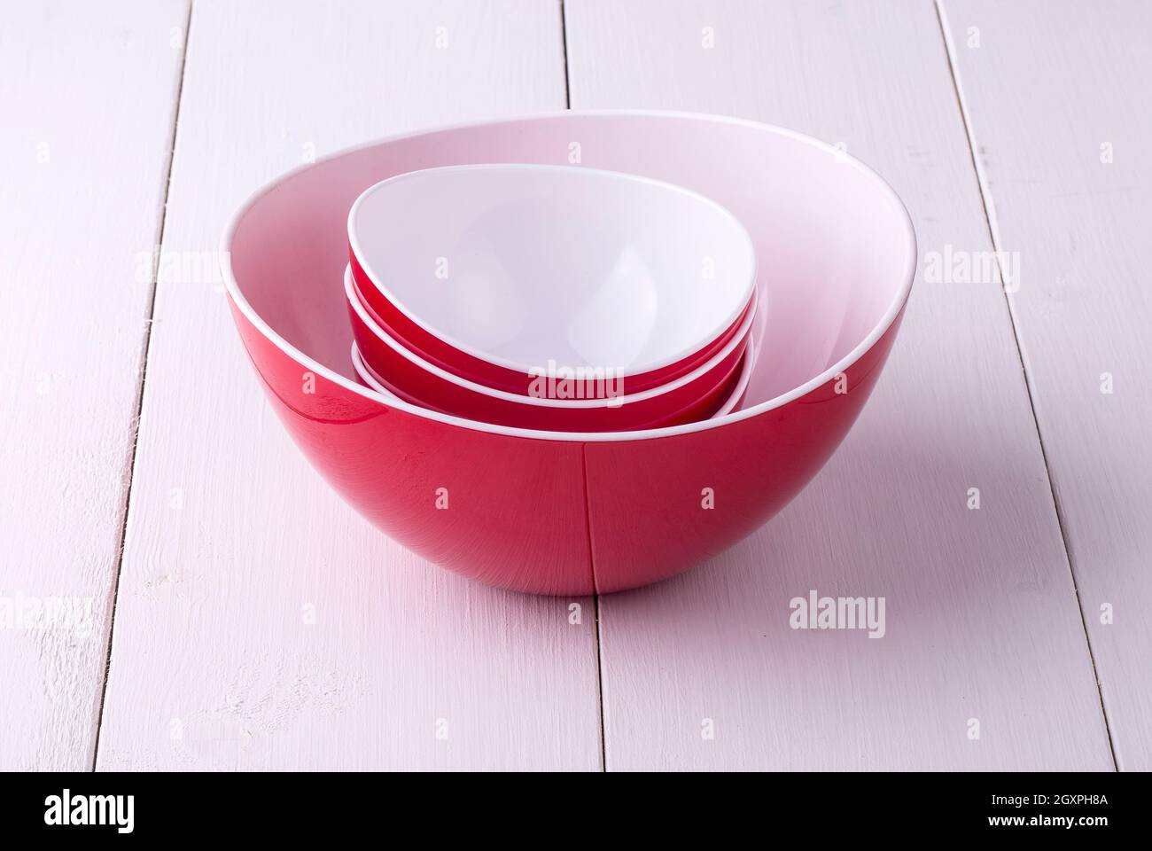 https://c8.alamy.com/comp/2GXPH8A/an-empty-red-salad-bowl-and-cups-on-a-white-wooden-table-2GXPH8A.jpg