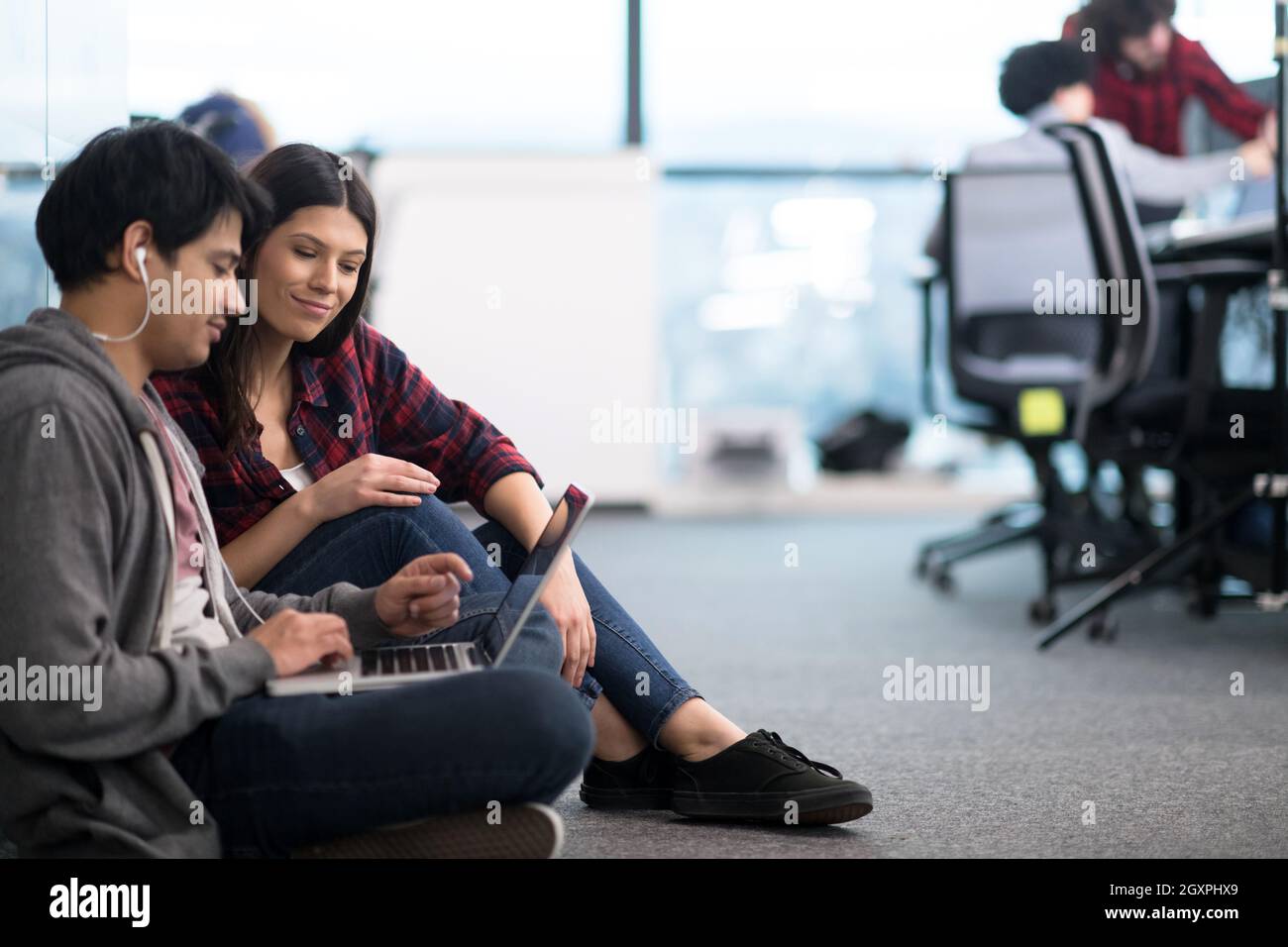 young software developers couple using laptop computer writing programming code while sitting on the floor at modern creative startup office Stock Photo