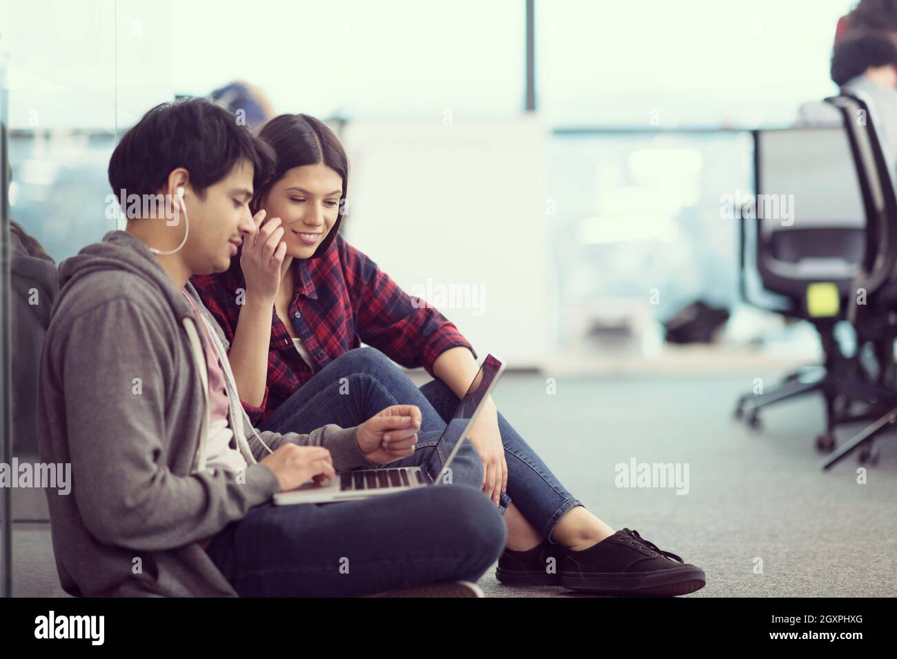 young software developers couple using laptop computer writing programming code while sitting on the floor at modern creative startup office Stock Photo