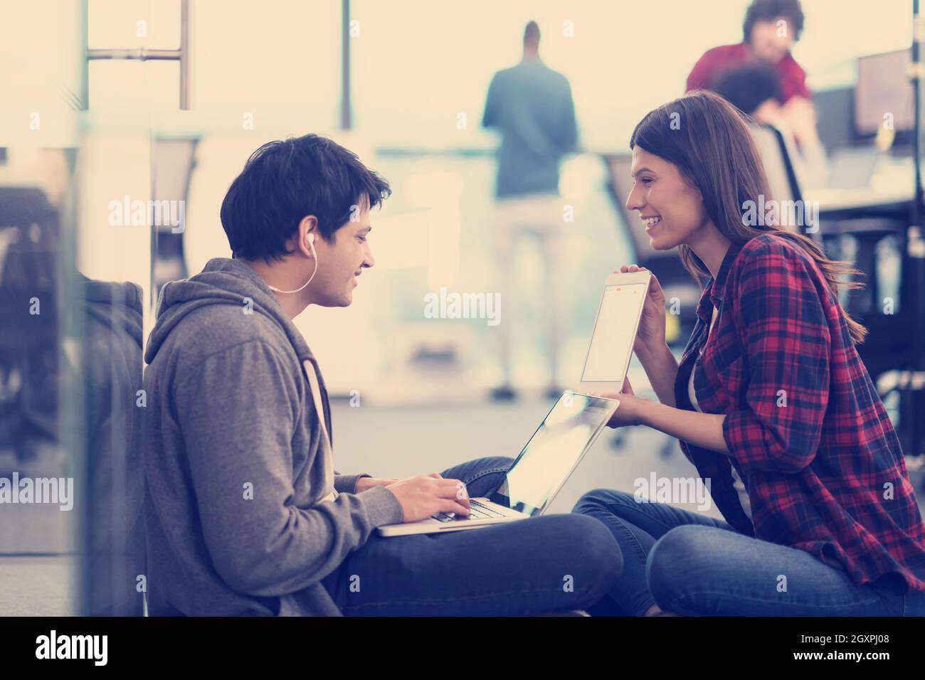 young software developers couple using laptop computer writing programming code while sitting on the floor at modern creative startup office Stock Photo