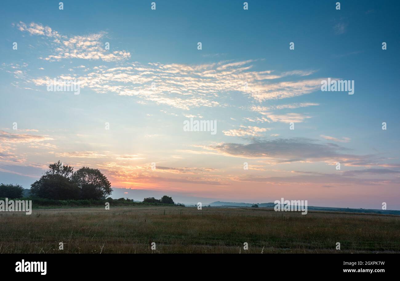 Dawn on a mid August morning as daybreaks with an orange glow and illuminated clouds, to greet the landscapes of Salisbury plains. Stock Photo