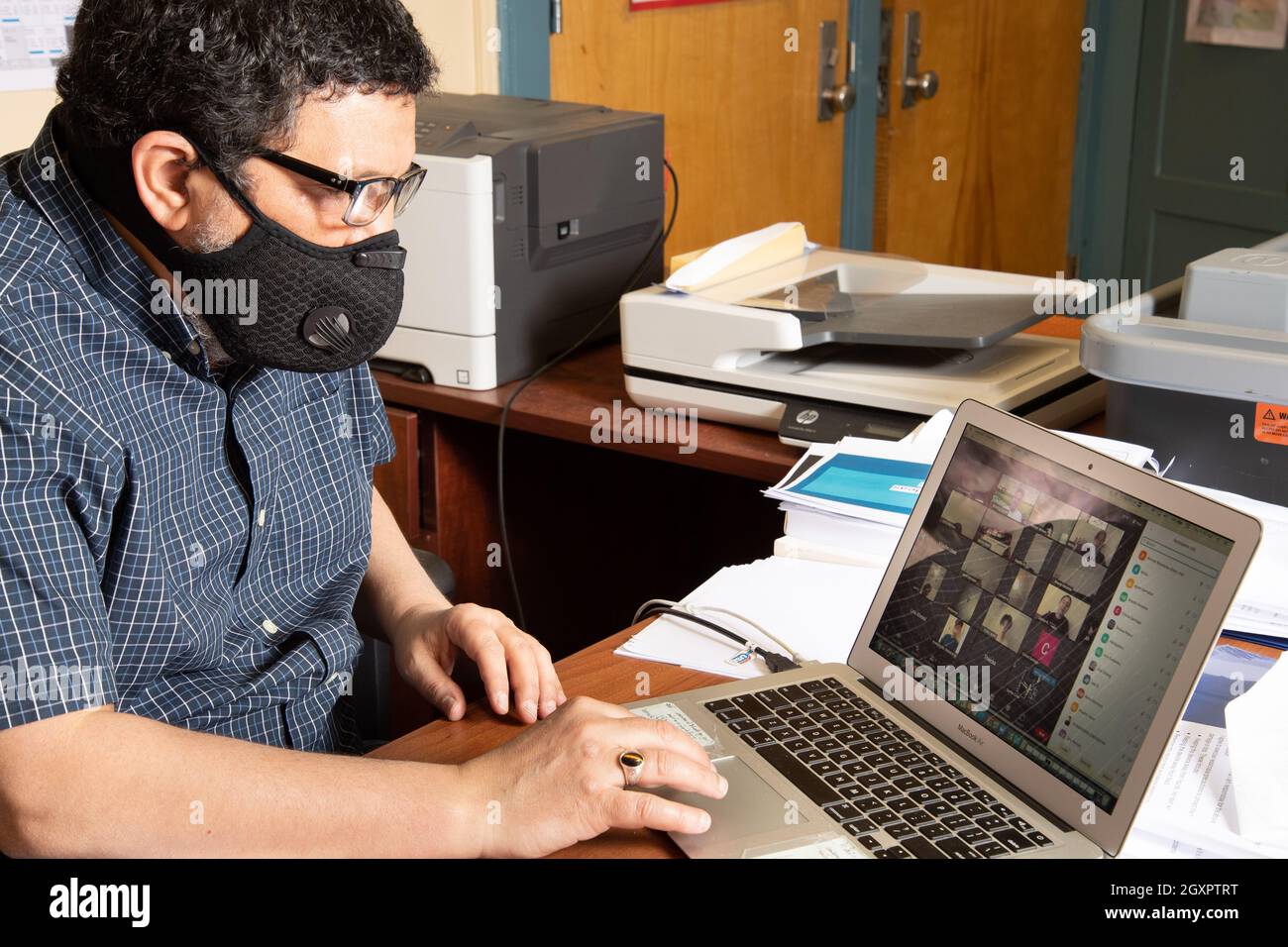 Education High School male teacher in face mask conducting class via Zoom on laptop computer during the Covid-19 pandemic Stock Photo