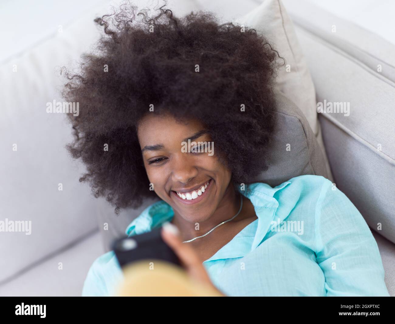 young happy african american woman sitting on sofa and using mobile ...