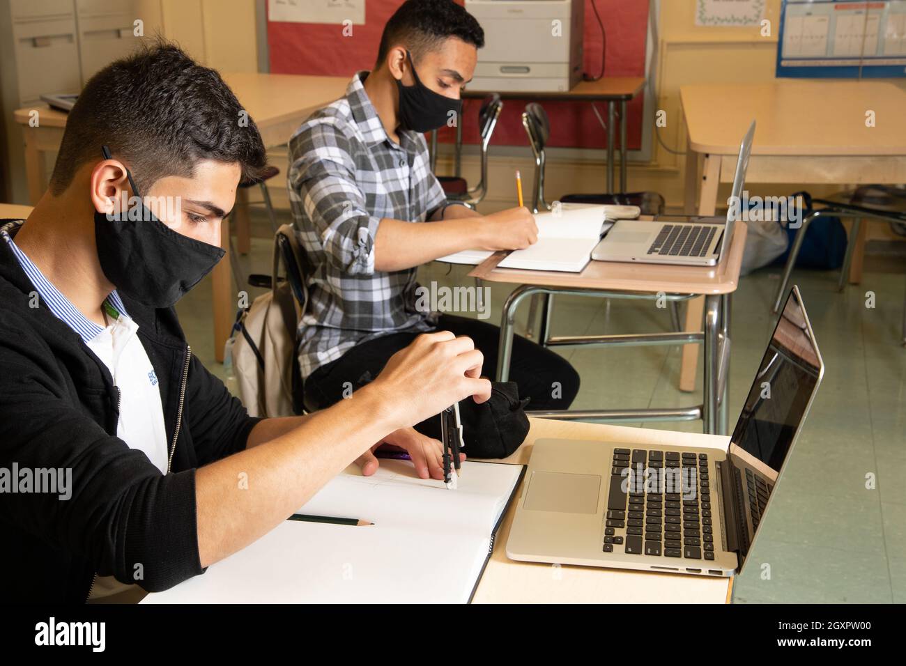 Education High School classroom scene two male students working in class, one using protractor, both with laptop computers on desks in front of them Stock Photo